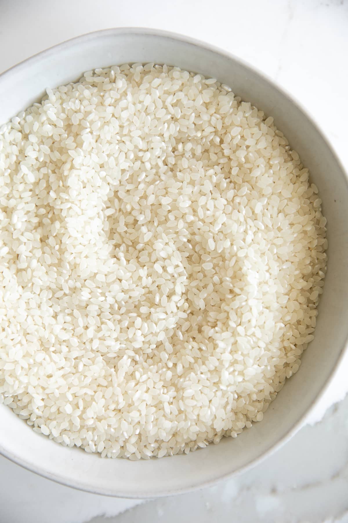 Uncooked glutinous sticky rice in a white bowl.