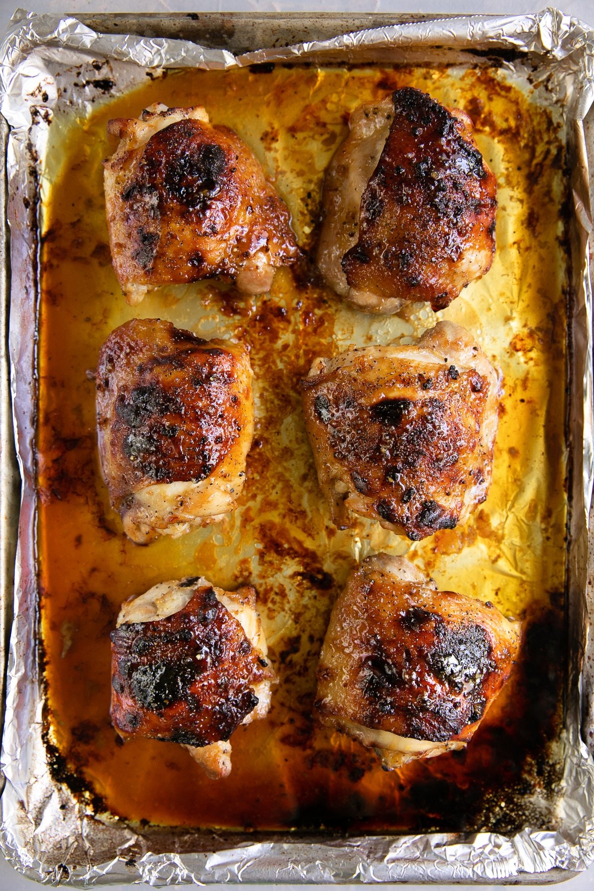 Large rimmed baking sheet with six cooked bone-in skin-on chicken thighs with honey soy marinade.