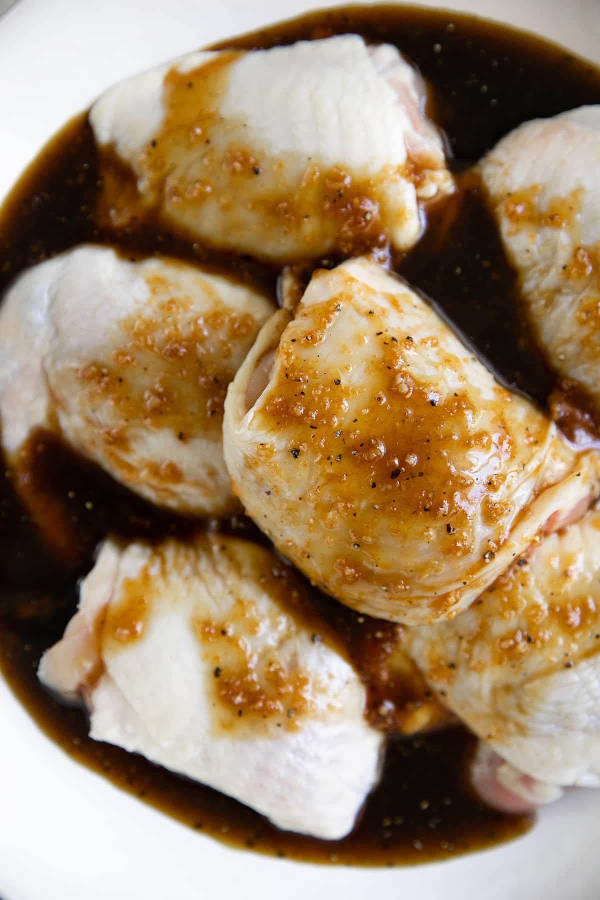 Large bone-in and skin-on chicken thighs placed in a large bowl filled with honey, soy, ginger, and garlic marinade.