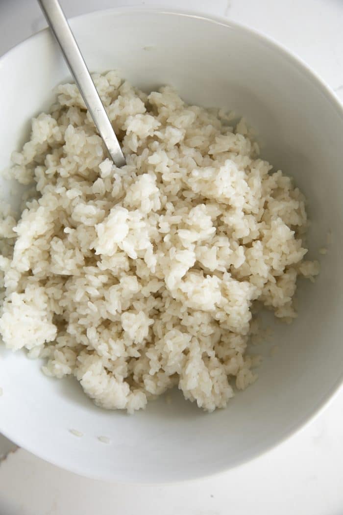Cooked sweet sticky rice in a large white bowl soaked in coconut milk and sugar.