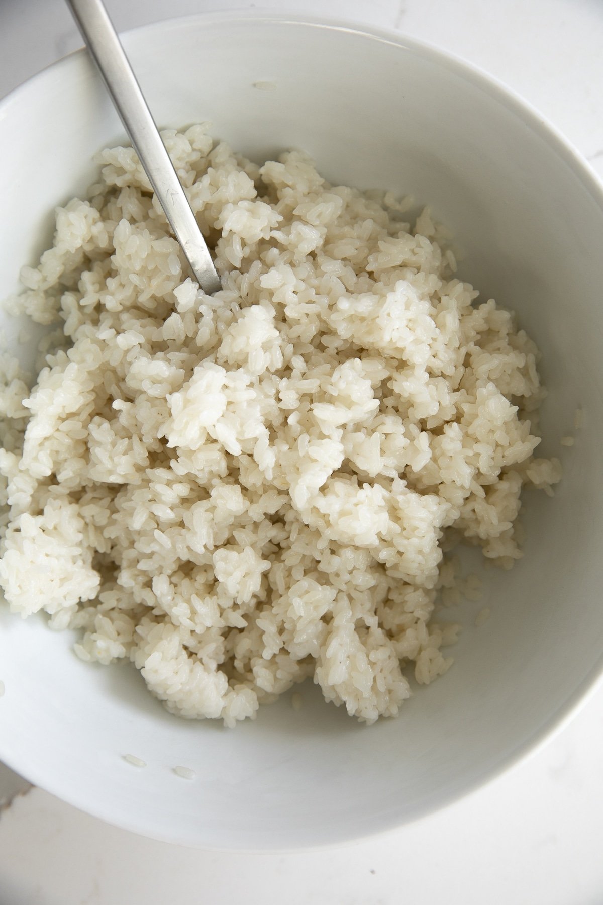 Cooked sweet sticky rice in a large white bowl soaked in coconut milk and sugar.