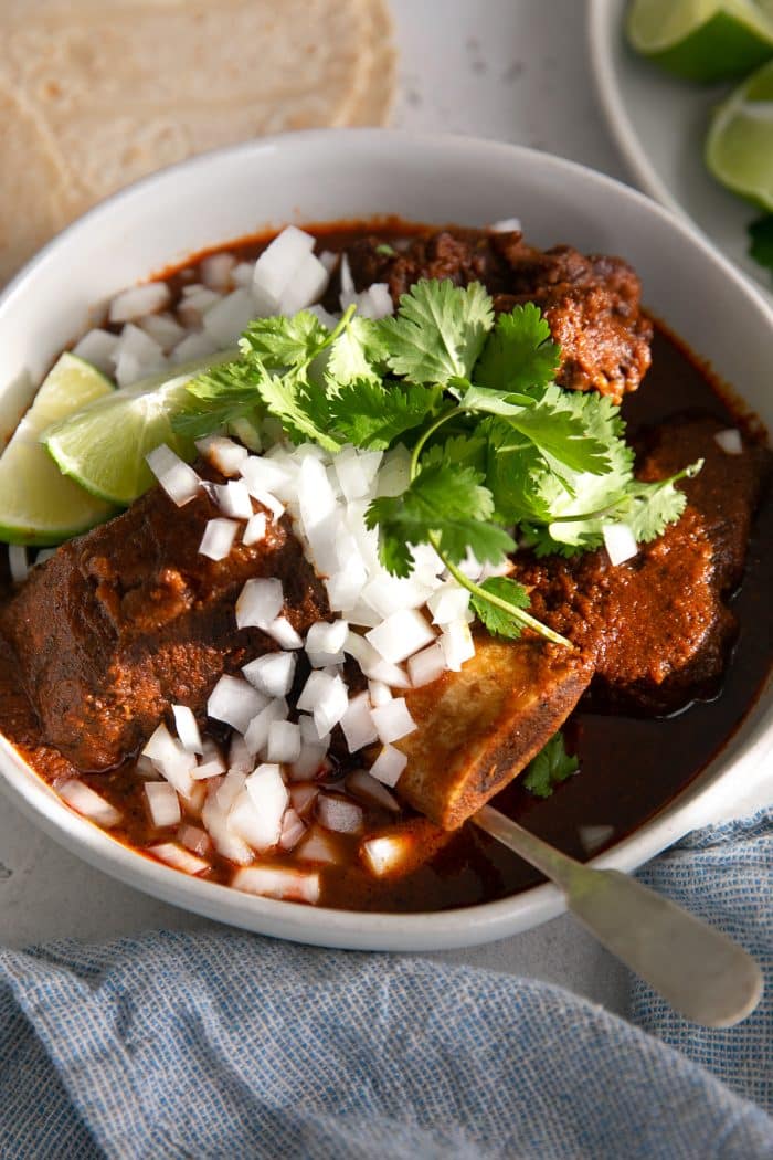 Bowl filled with cooked beef birria garnished with white onion, cilantro, and lime wedges.
