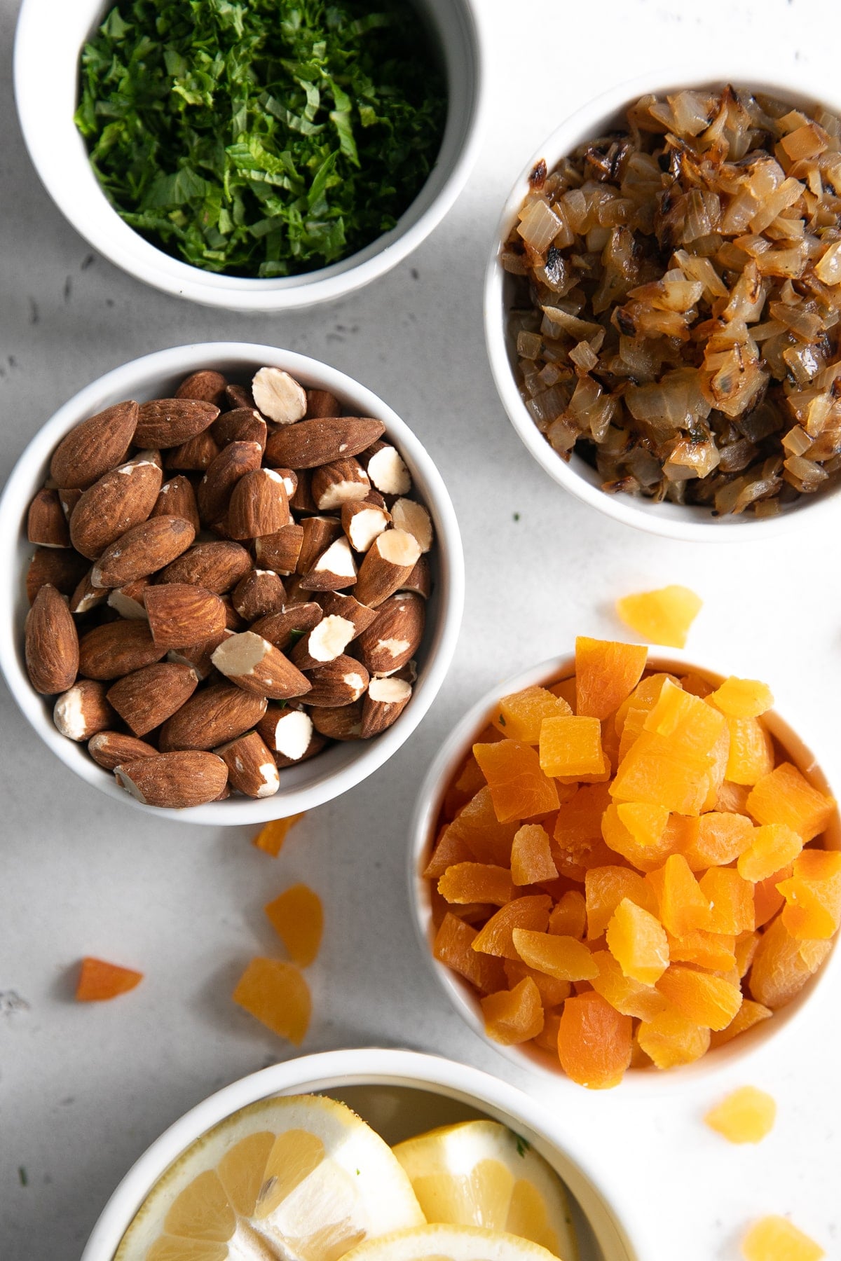 Fresh herbs, caramelized onions, almonds, chopped dried apricots, and butter in individual serving dishes.