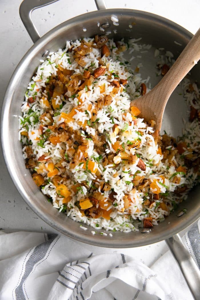 Overhead image of a large saute pan filled with cooked basmati rice mixed with caramelized onions, herbs, almonds, dried apricots, and lemon juice.