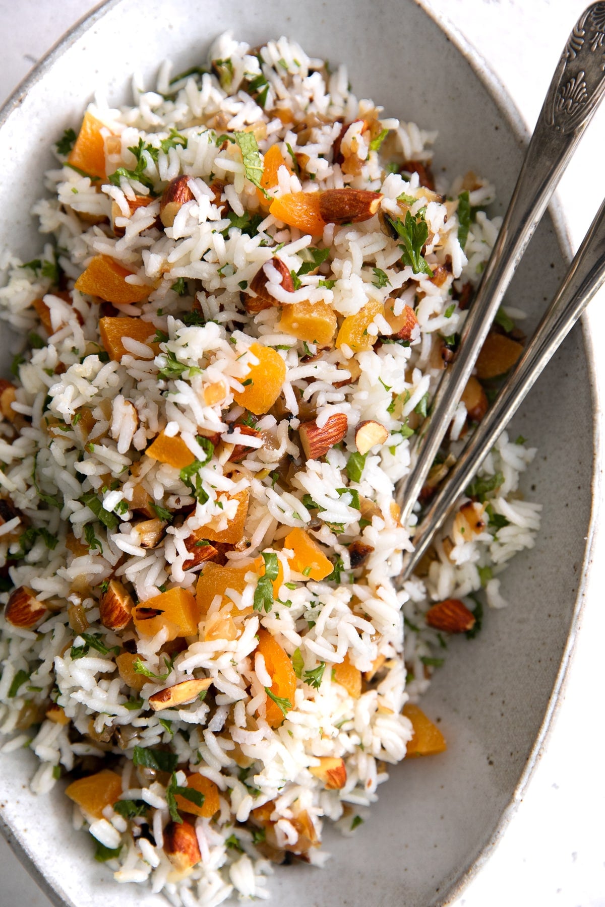 Easy basmati rice recipe in a large serving dish and topped with fresh herbs, almonds, dried apricots, and caramelized onions.