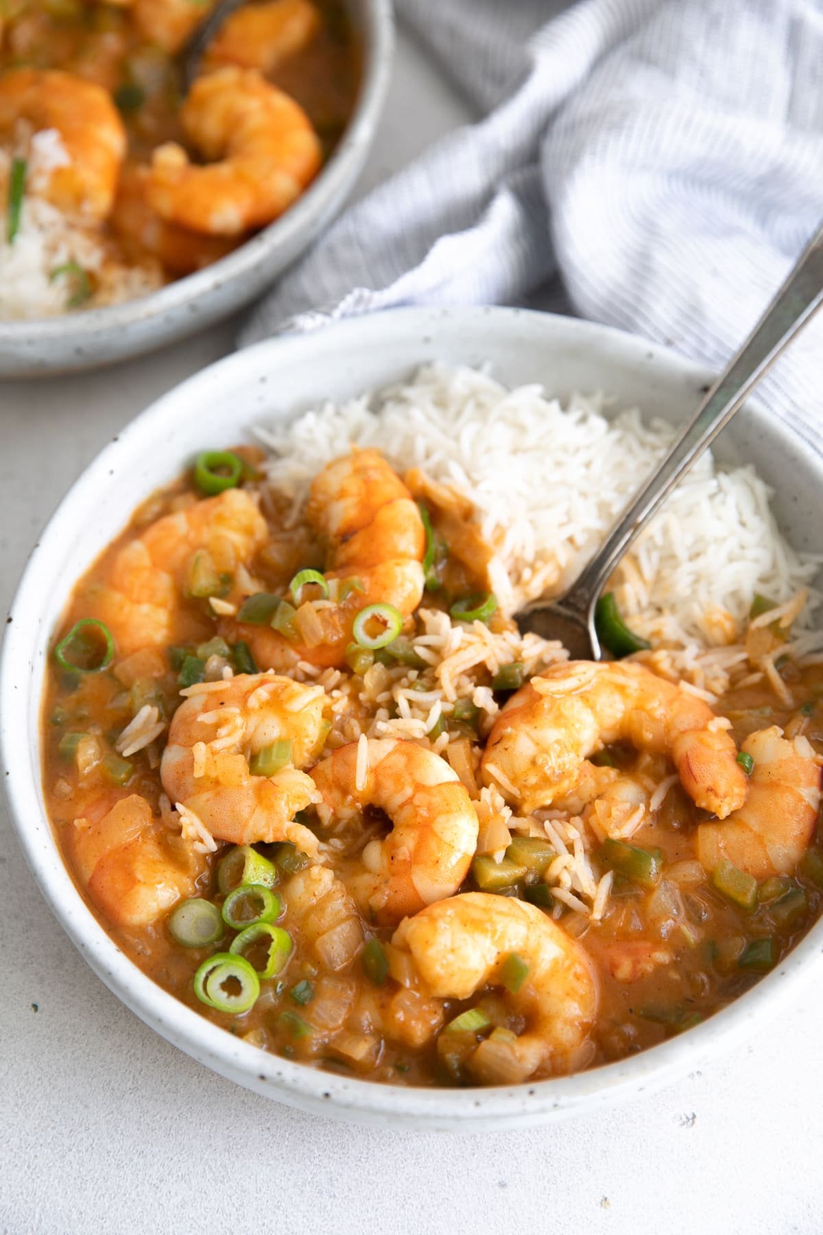 White serving bowl filled with cooked shrimp etouffee with a serving of cooked white rice.