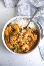 White serving bowl filled with cooked shrimp etouffee with a serving of cooked white rice.