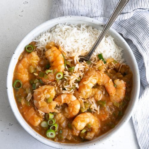 White serving bowl filled with cooked shrimp etouffee with a serving of cooked white rice.