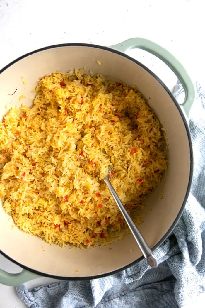 Fork fluffing a large pot of yellow-colored spanish rice.