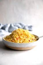 Bowl filled with yellow cooked rice dotted with small pieces of red bell peppers.