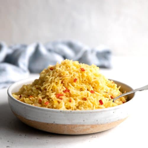 Bowl filled with yellow cooked rice dotted with small pieces of red bell peppers.