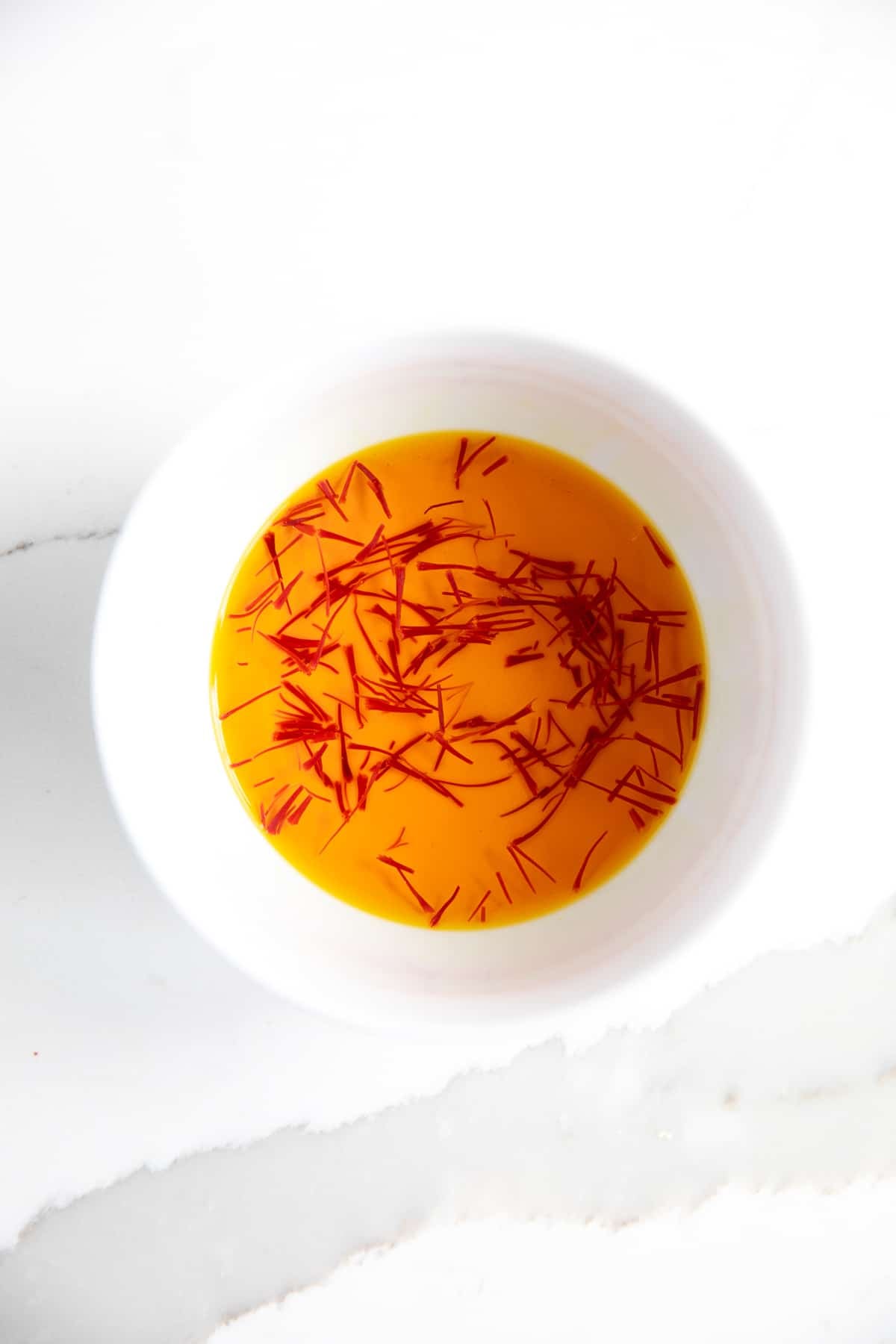 Small white bowl filled with threads of saffron steeping in warm water.
