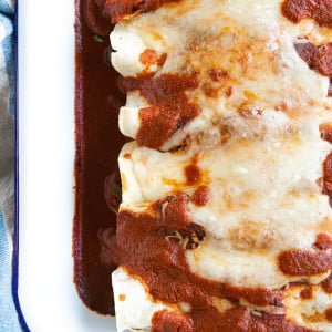 White baking dish filled with vegetarian enchiladas topped with enchilada sauce and melted cheese.