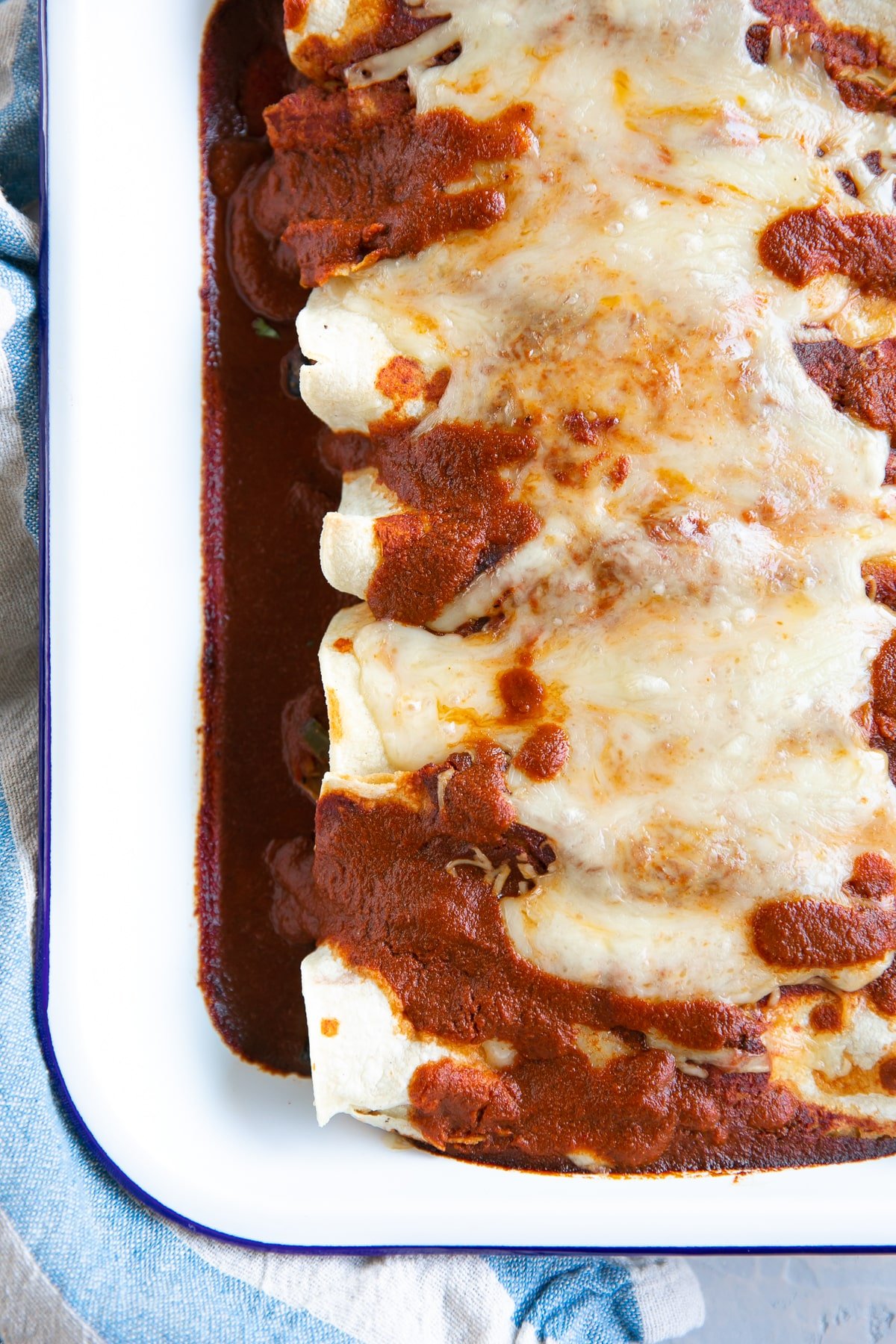 White baking dish filled with vegetarian enchiladas topped with enchilada sauce and melted cheese.