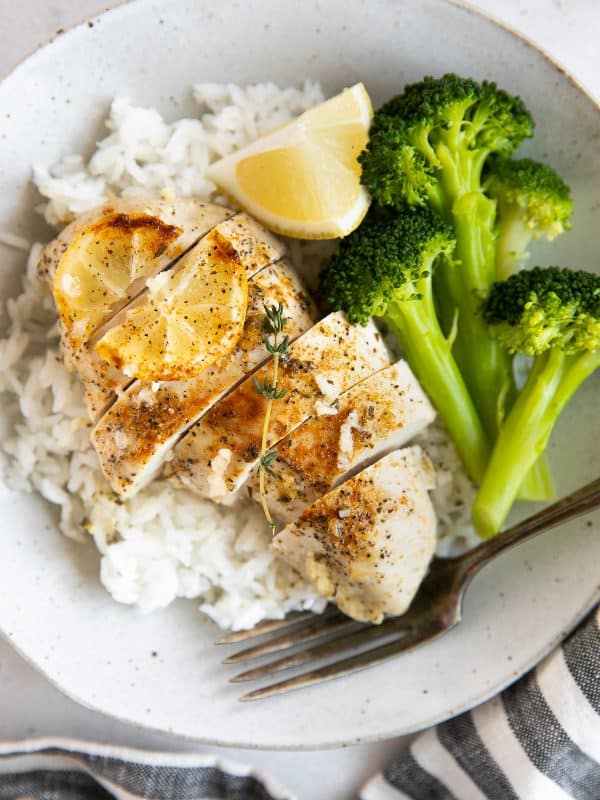 Baked lemon chicken breast sliced on a plate with rice and broccoli.