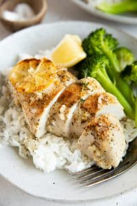 Sliced baked lemon chicken served over rice with steamed broccoli and lemon wedges.