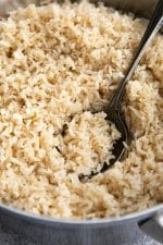 Spoon scooping cooked brown rice from a medium stockpot.