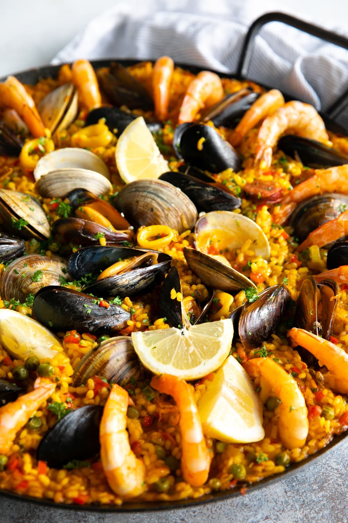 Spanish paella recipe in a large paella pan garnished with lemon wedges and chopped parsley.
