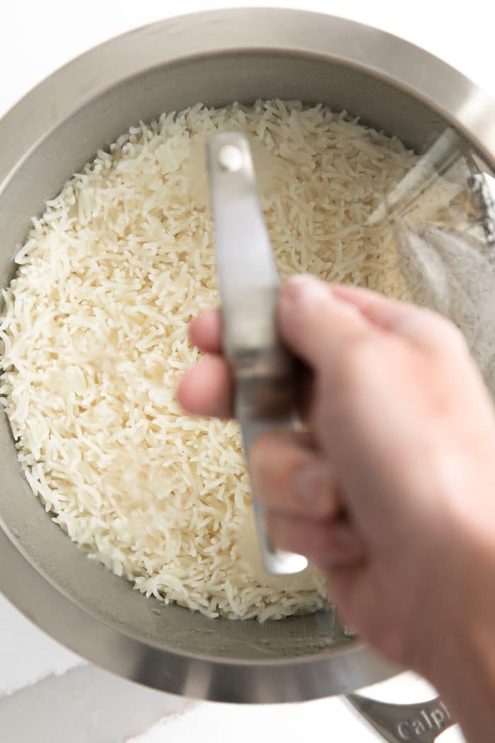 Perfectly cooked basmati rice in a small pot covered with a glass lid held by it's handle by a hand.