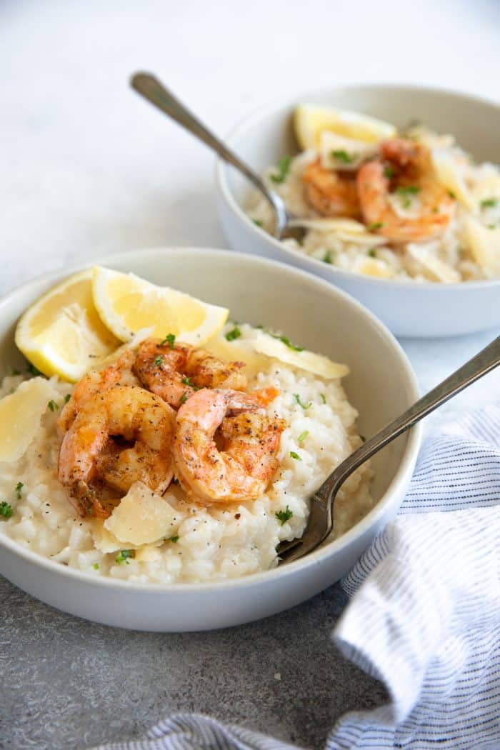 two white bowls of Creamy Parmesan Risotto Recipe with Shrimp with slice of lemon surrounded by blue striped napkin