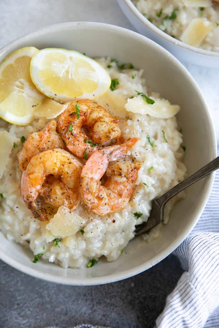 overhead image of white bowl of Creamy Parmesan Risotto Recipe with Shrimp with slice of lemon surrounded by blue striped napkin