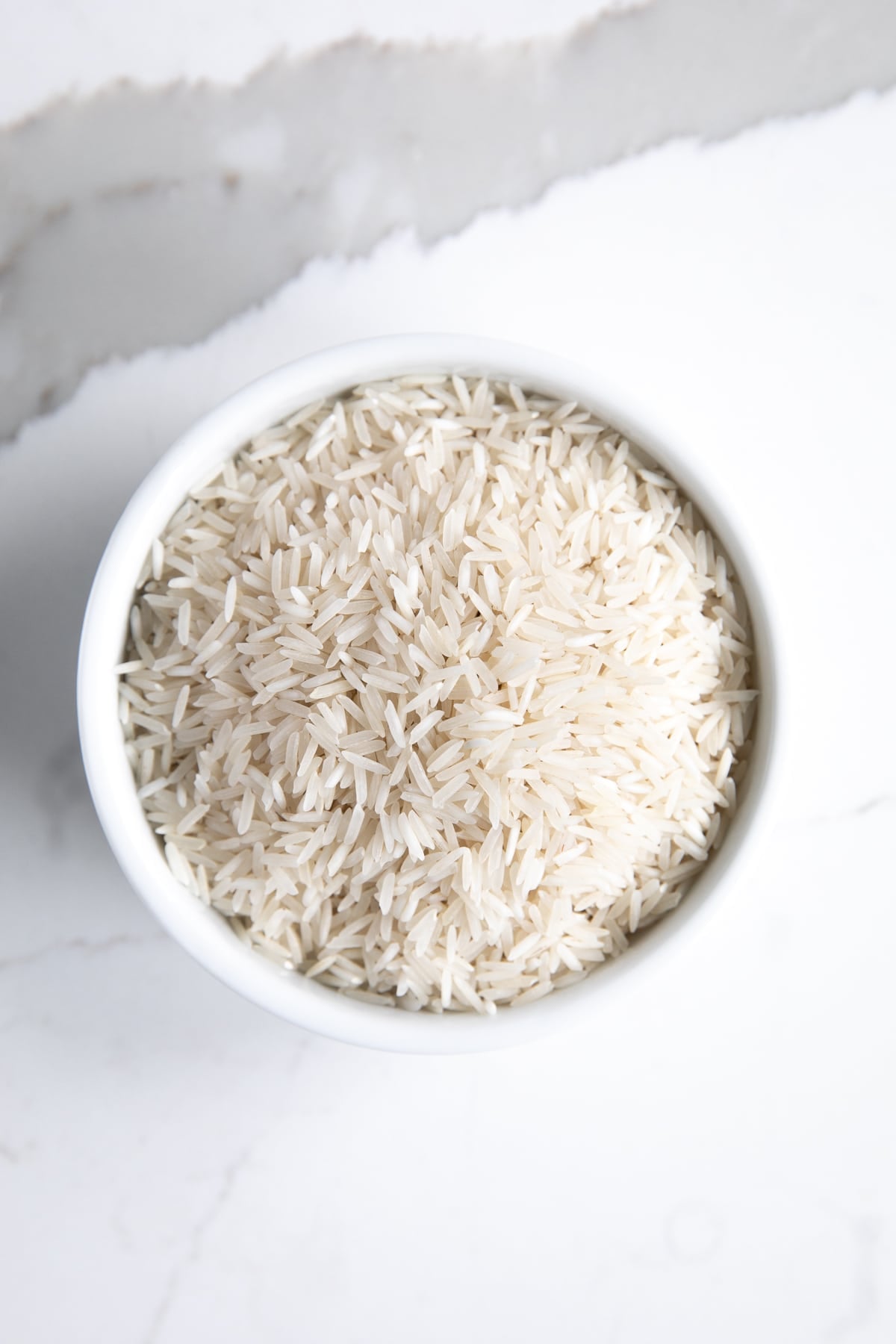 White bowl filled with uncooked basmati rice.