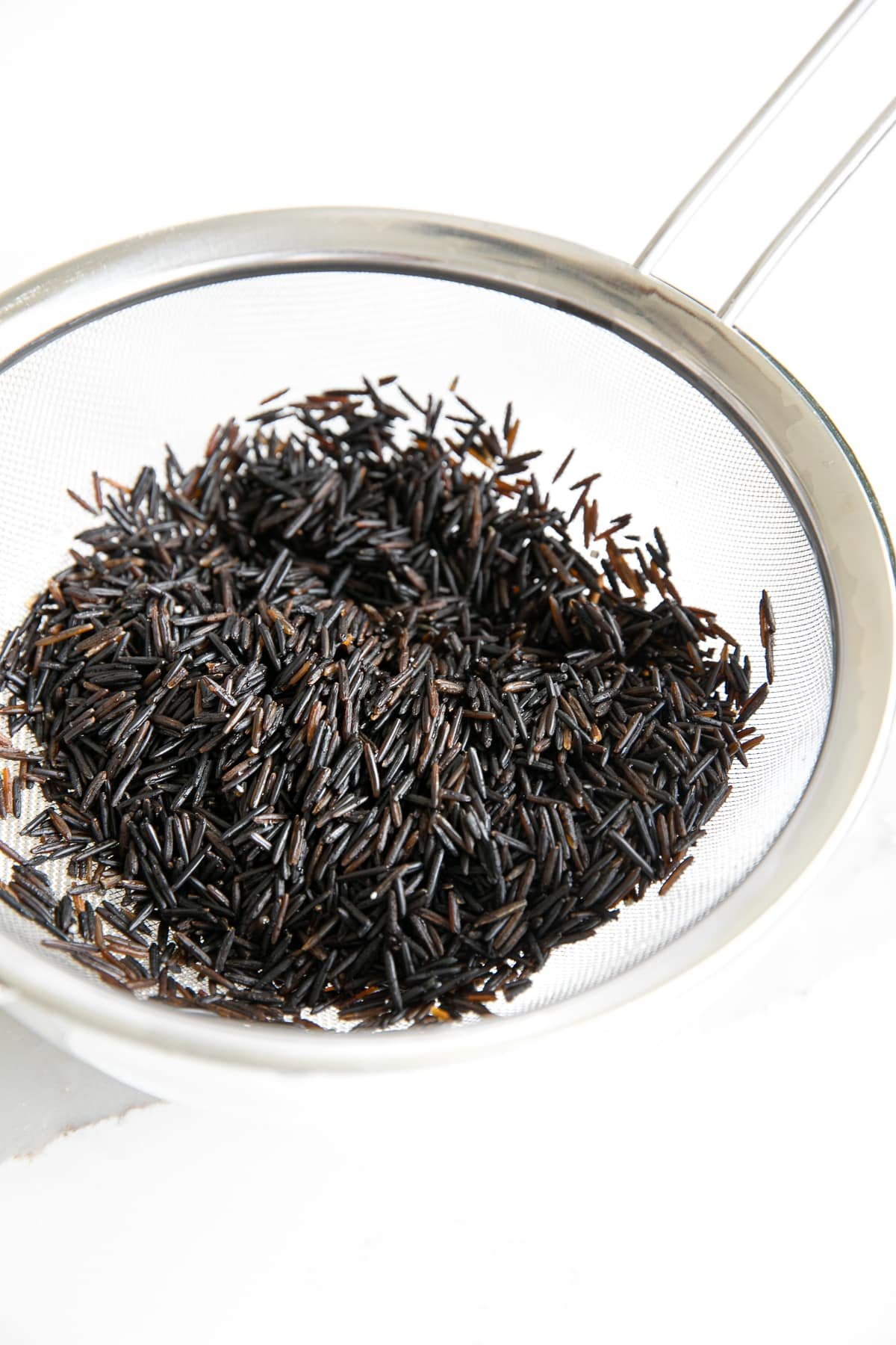 Fine-mesh strainer resting over a glass bowl and filled with wild rice.