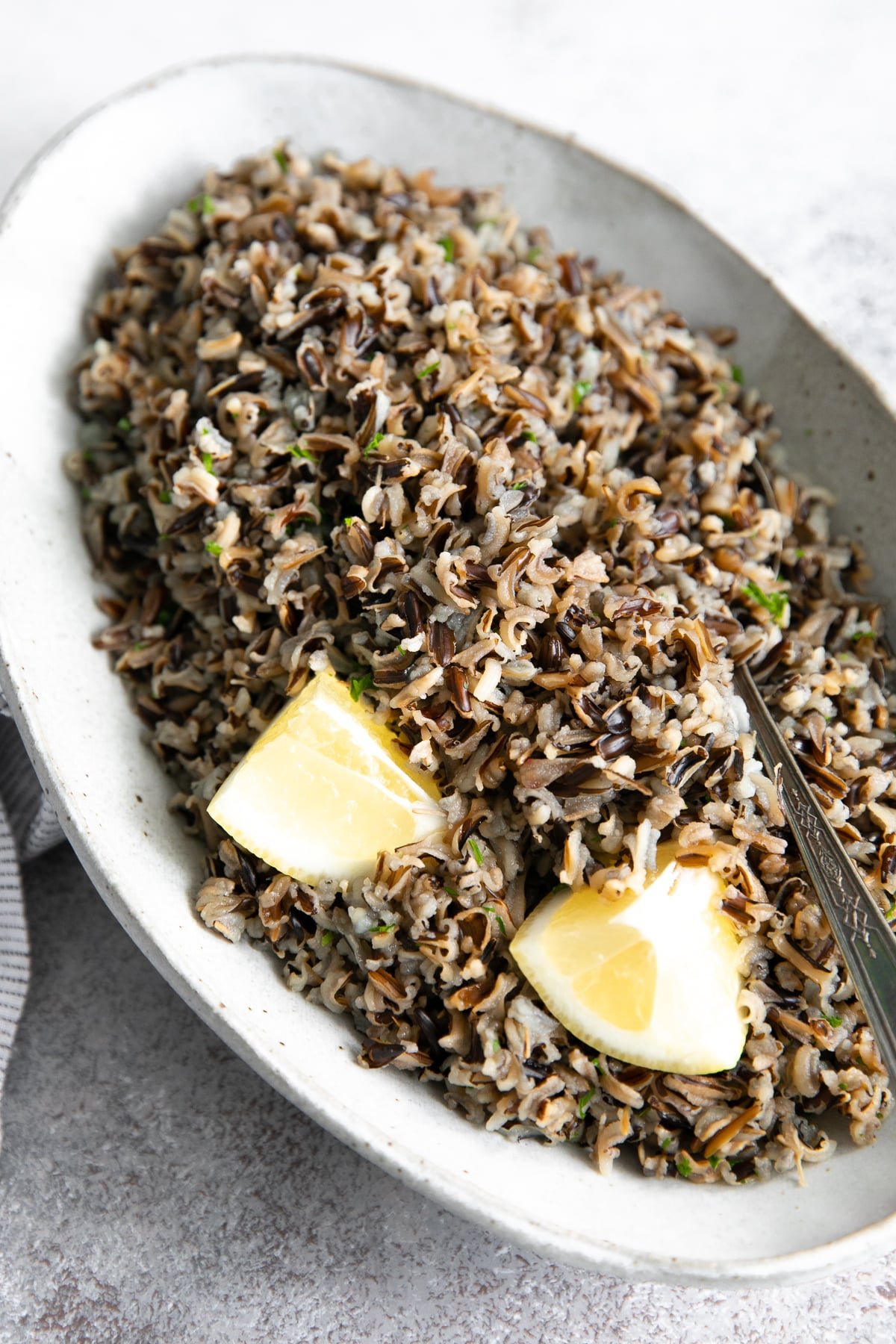 Oval-shaped serving dish filled with cooked wild rice garnished with fresh parsley and lemon wedges.