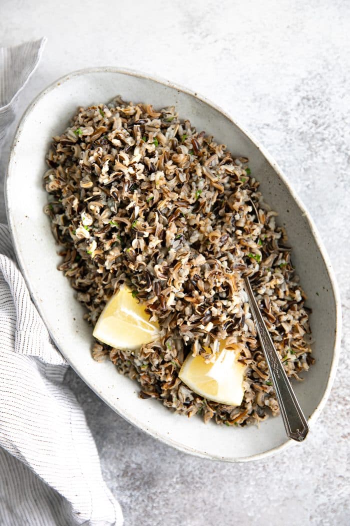 Oval-shaped serving dish filled with cooked wild rice garnished with fresh parsley and lemon wedges.