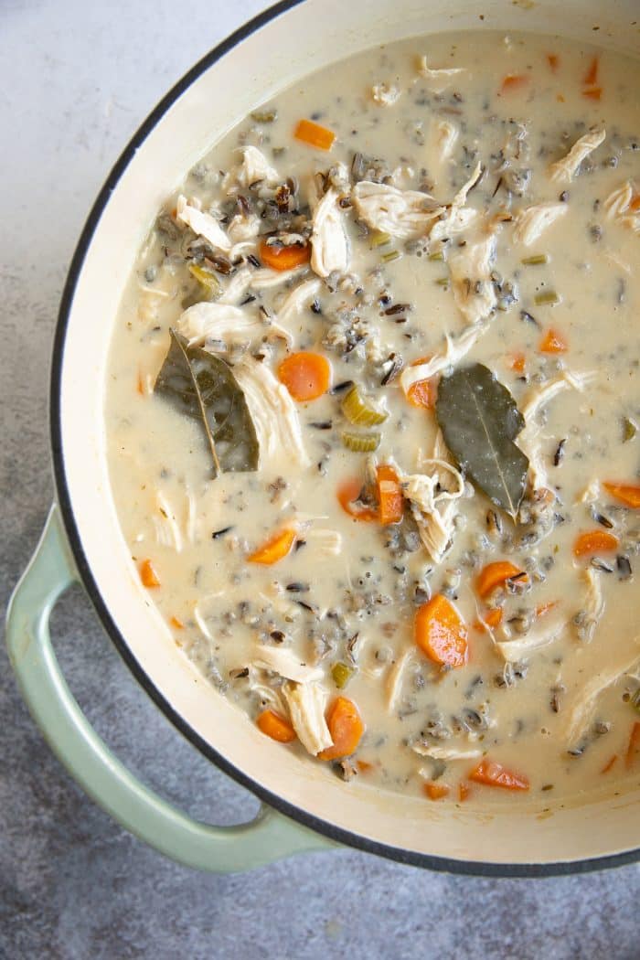 Large Dutch oven filled with creamy soup made with wild rice, carrots, shredded chicken, celery, and seasoned with fresh thyme and bay leaves.