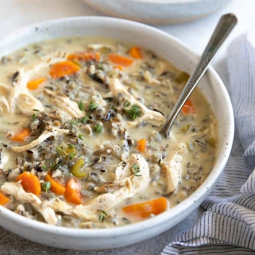 Shallow white serving bowls filled with chicken and with wild rice soup made with carrots, onion, celery, chicken, and cream.
