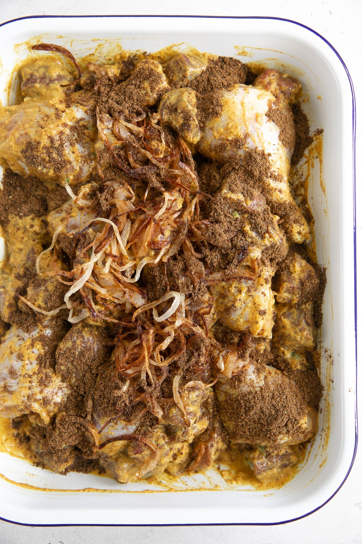 Chicken and lamb marinating in yogurt and spices in a large baking dish.