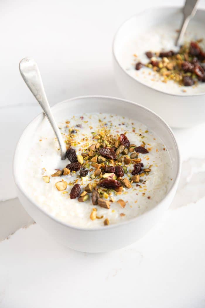 Small white dessert bowls filled with cardamom spiced Indian Indian kheer recipe and garnished with crushed pistachios and raisins.
