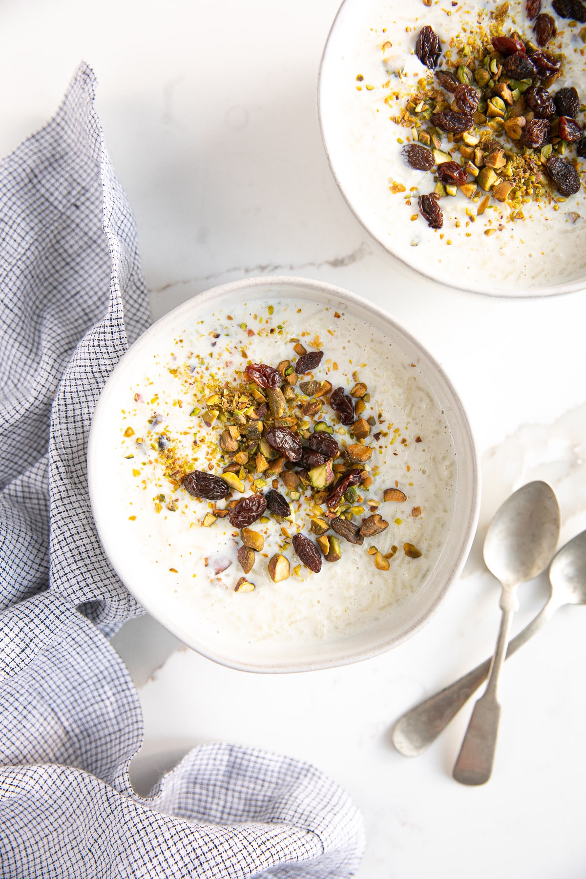 Two white bowls filled with kheer and topped with crushed pistachios and raisins.