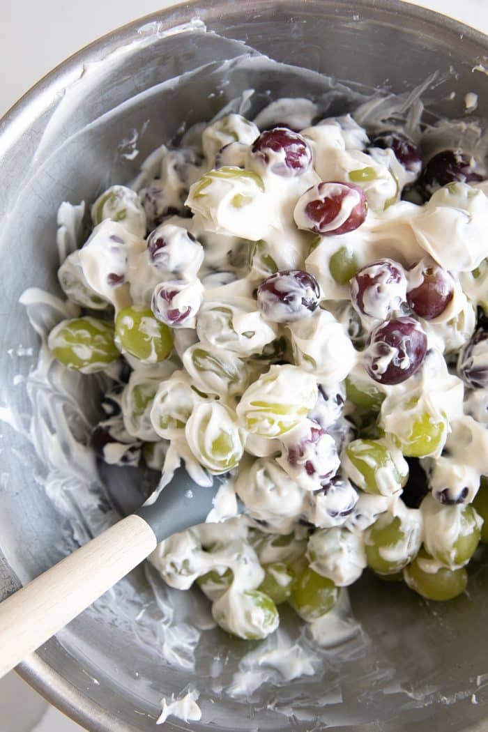 Large mixing bowl filled with red and green grapes and mixed with creamy cheese and sour cream.