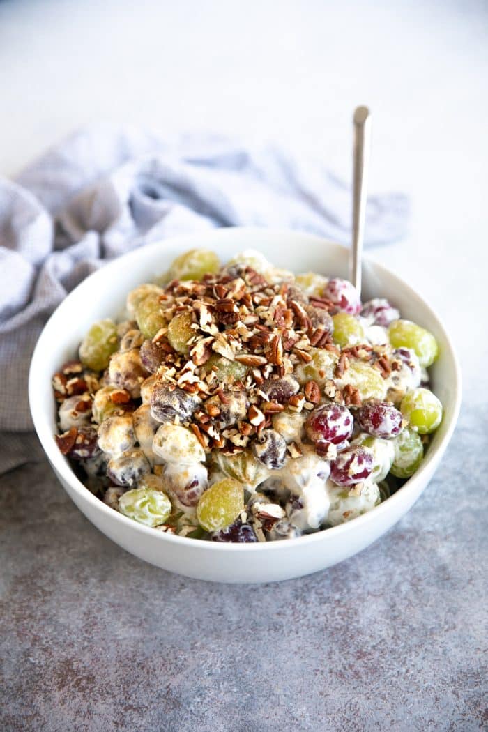 Large white serving bowl filled with red and green grapes mixed with cream cheese, sugar, sour cream, vanilla extract, and chopped pecans.