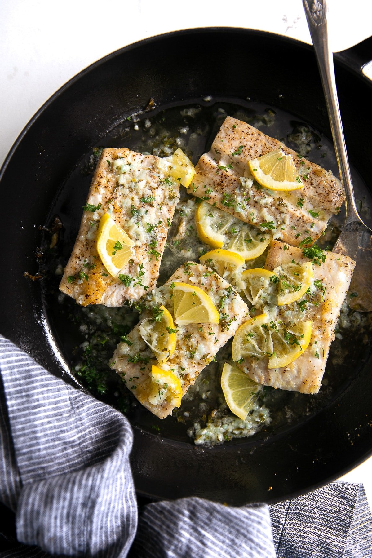 Four mahi mahi fillets in a large skillet covered with a homemade lemon butter sauce and garnished with fresh parsley.