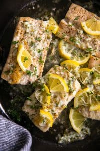 Skillet filled with fully cooked mahi mahi fillets cooked in a lemon butter sauce and garnished with fresh parsley.