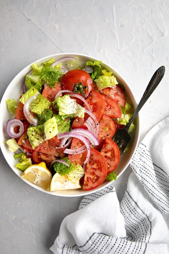 Large serving platter filled with sliced tomatoes, Romaine lettuce, sliced red onion, and homemade vinaigrette.