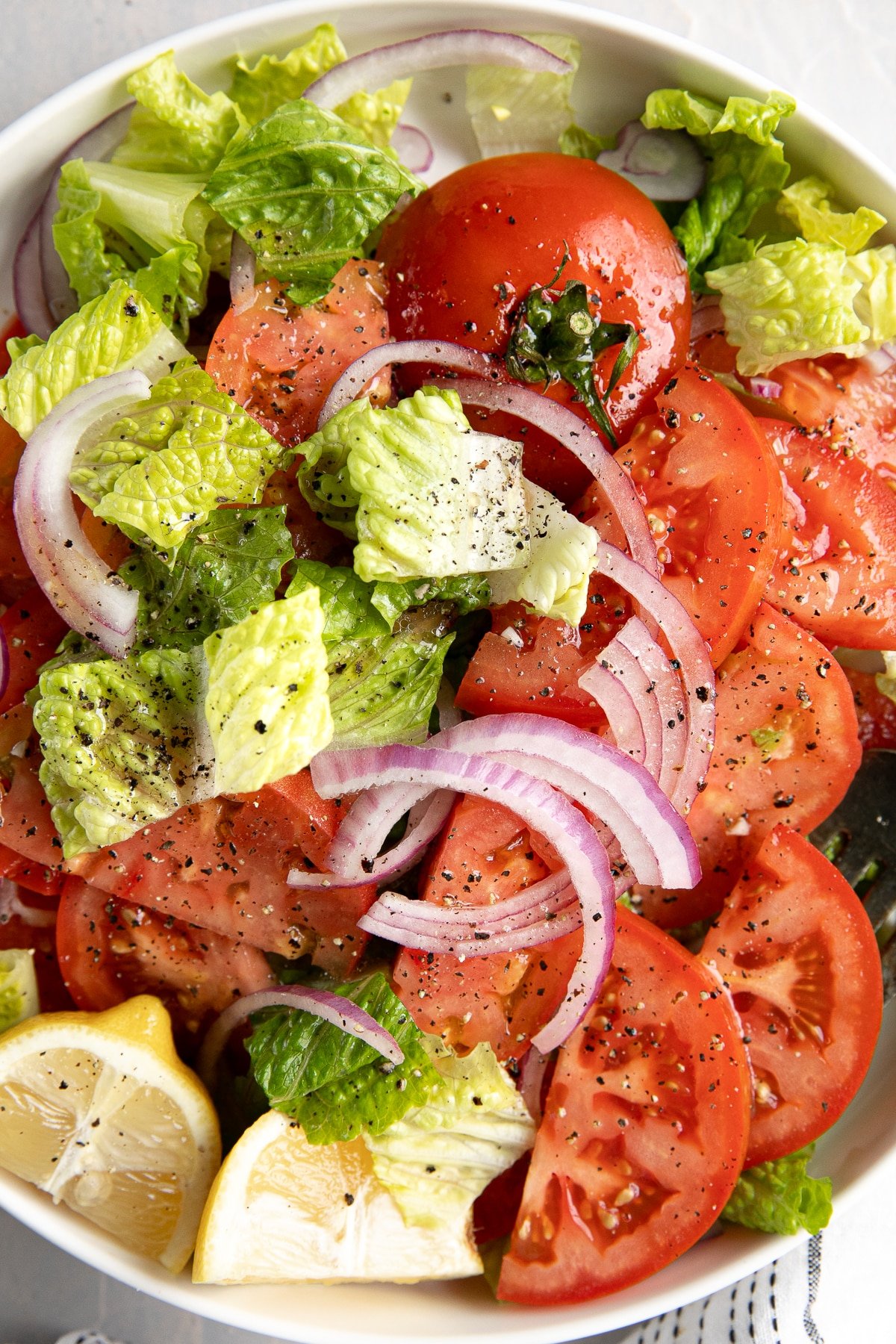 Close-up overhead image of fresh summer tomatoes sliced and served with chopped romaine lettuce and sliced red onions all drizzled with homemade vinaigrette.