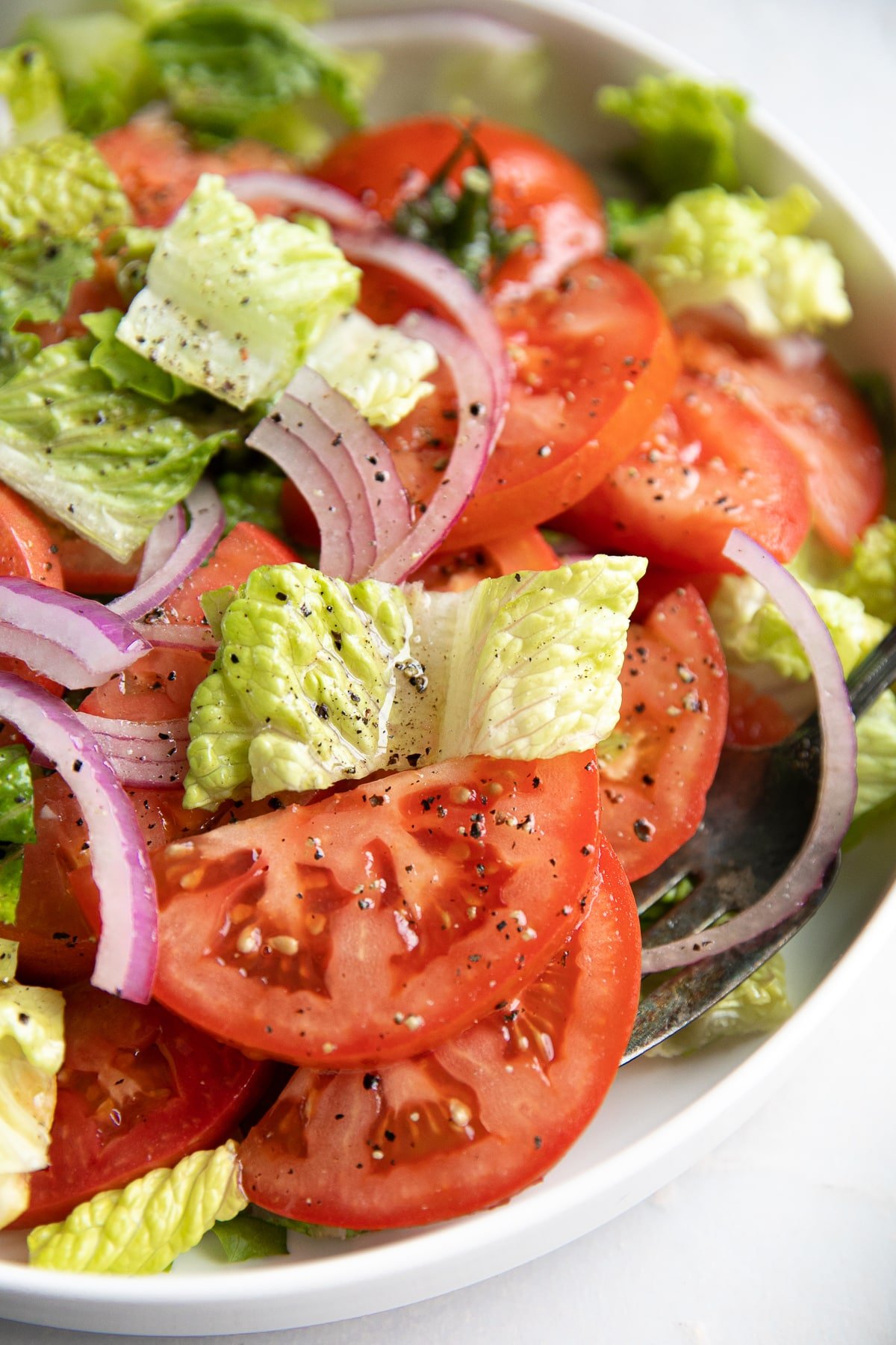 Large serving platter filled with sliced tomatoes, Romaine lettuce, sliced red onion, and homemade vinaigrette.