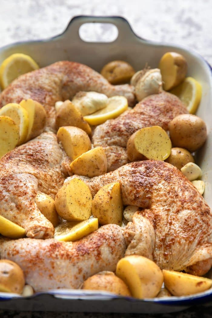 Raw chicken legs and potatoes in a large baking pan seasoned with salt, pepper, paprika, garlic powder, and onion powder.