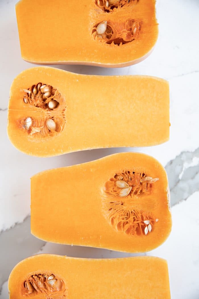 Four butternut squash halves cut-side-up in a row side by side.