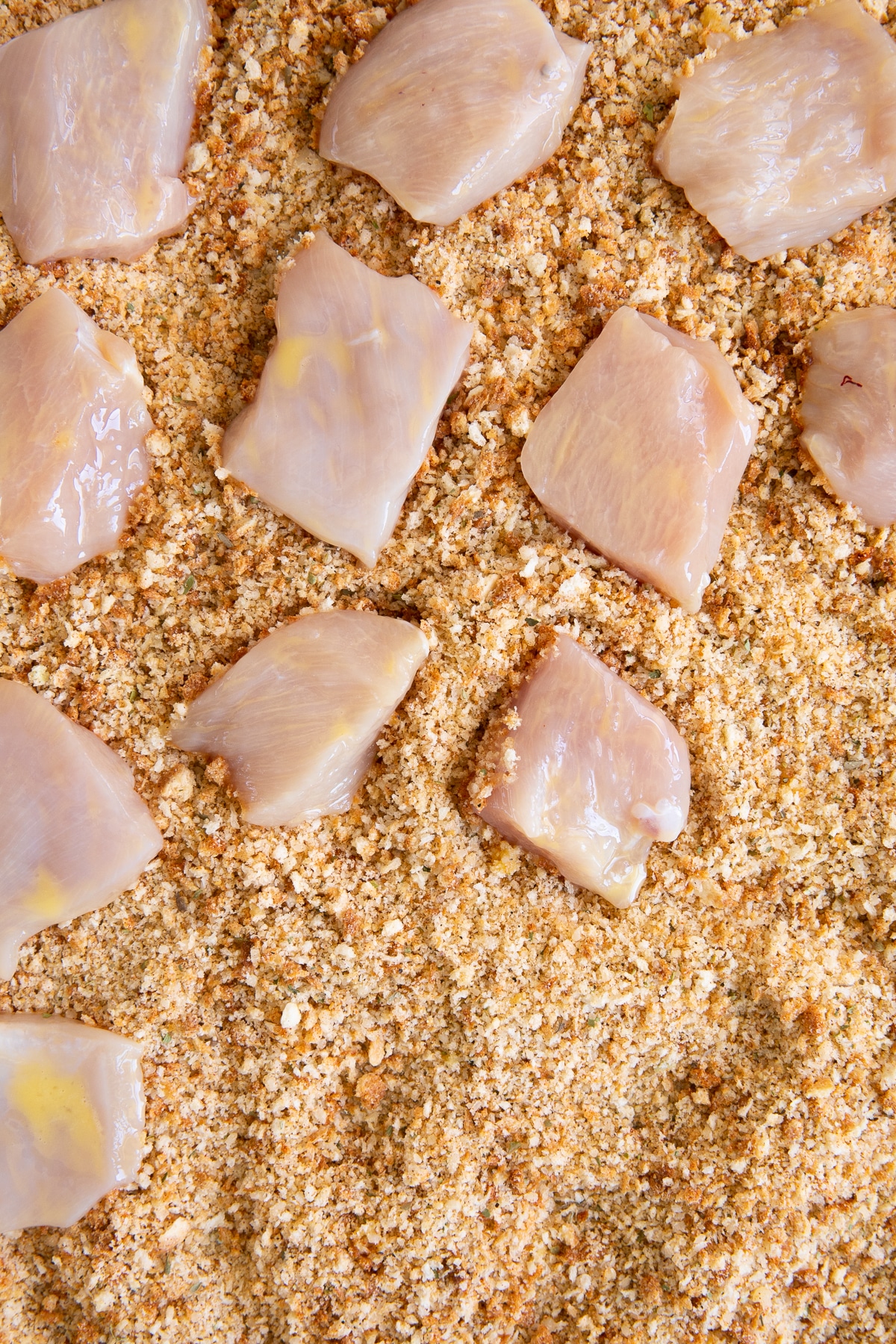 Coating raw chicken pieces in toasted panko breadcrumbs.