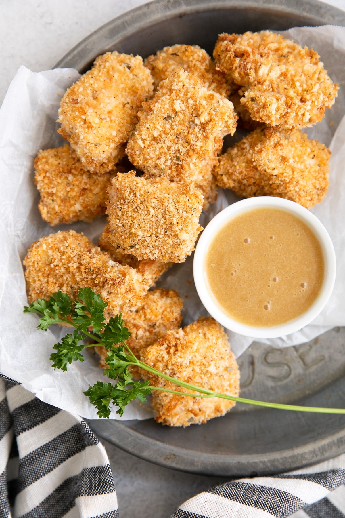 Small tray lined with parchment paper and filled with homemade baked chicken nuggets with a side of honey mustard sauce for dipping.