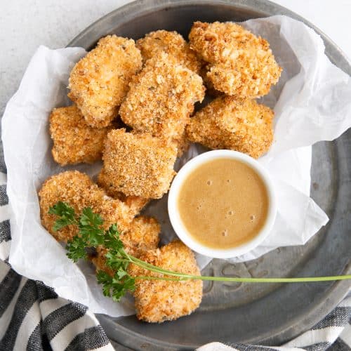 Small tray lined with parchment paper and filled with homemade baked chicken nuggets with a side of honey mustard sauce for dipping.