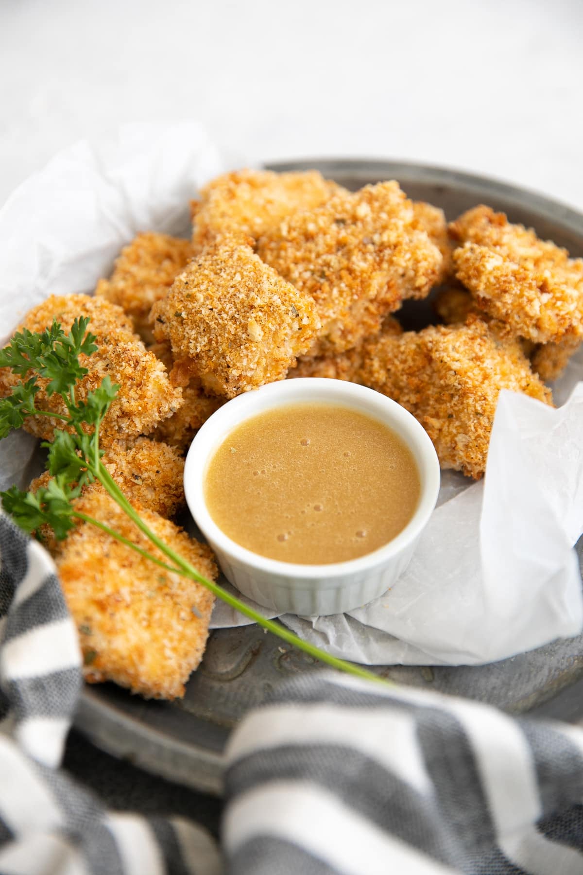 Small tray lined with parchment paper and filled with homemade baked chicken nuggets with a side of honey mustard sauce for dipping.