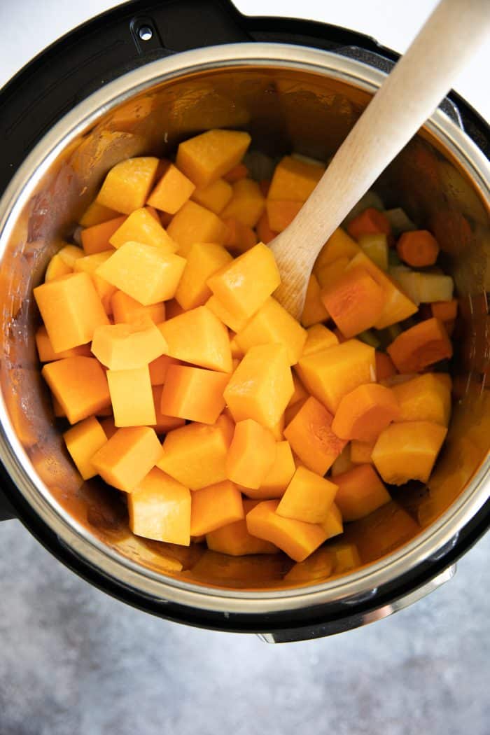 Cooked vegetables and raw butternut squash cubes in a large Instant Pot