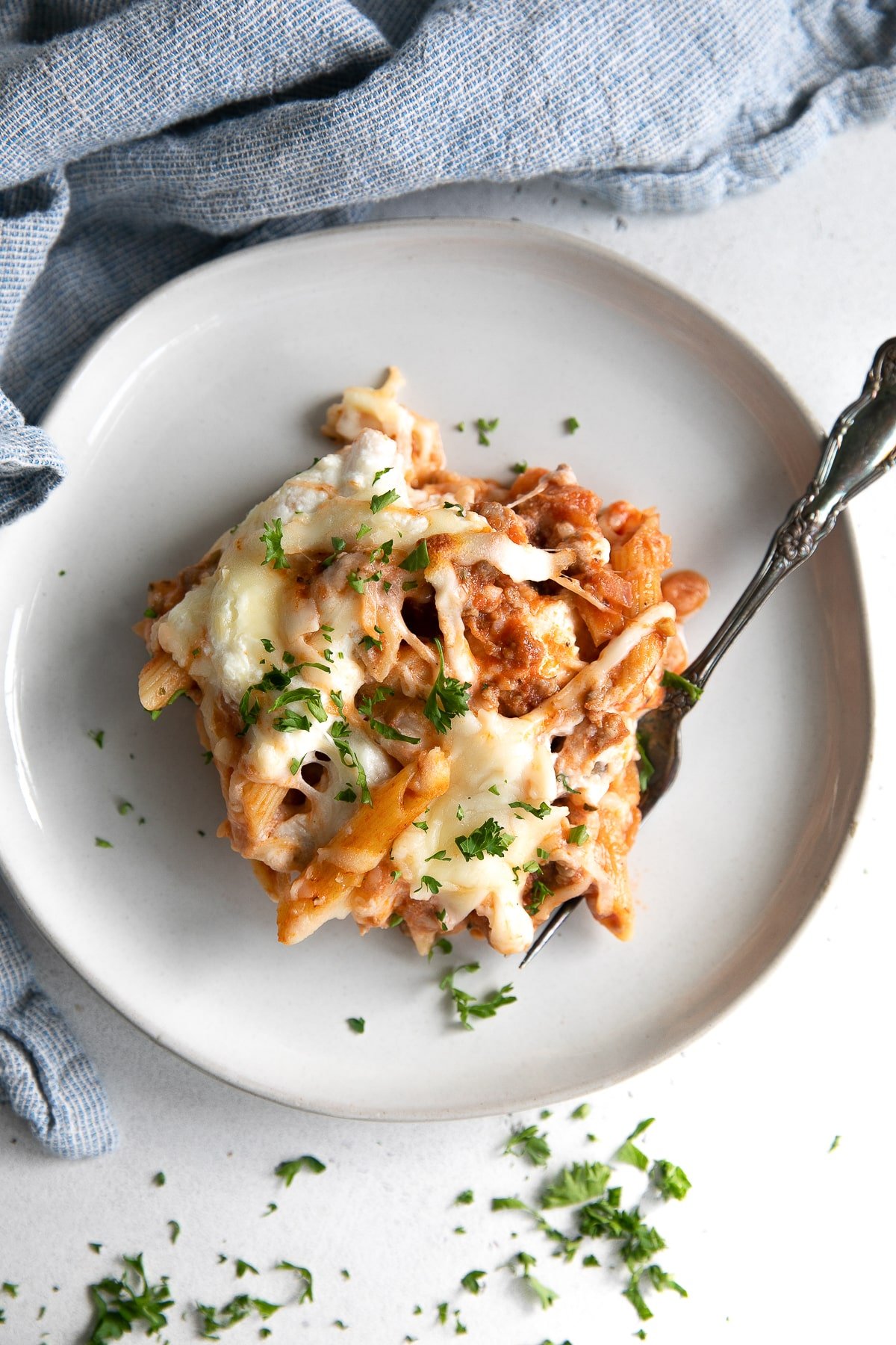 Single serving of baked mostaccioli on a small white serving plate covered with freshly chopped parsley.