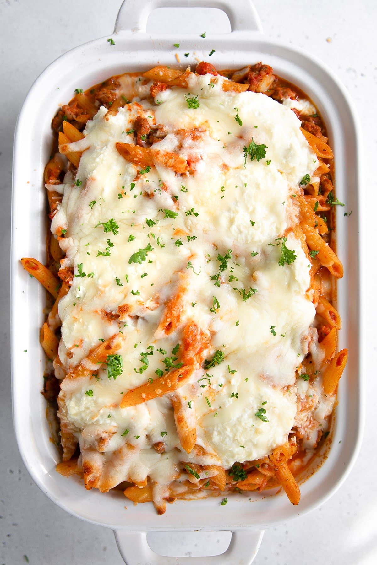 Large white baking dish filled with cheese covered and baked mostaccioli cooked in an Italian sausage and tomato pasta sauce.